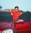 man in red and black hoodie standing beside red car during daytime