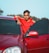 man in red and black hoodie standing beside red car during daytime