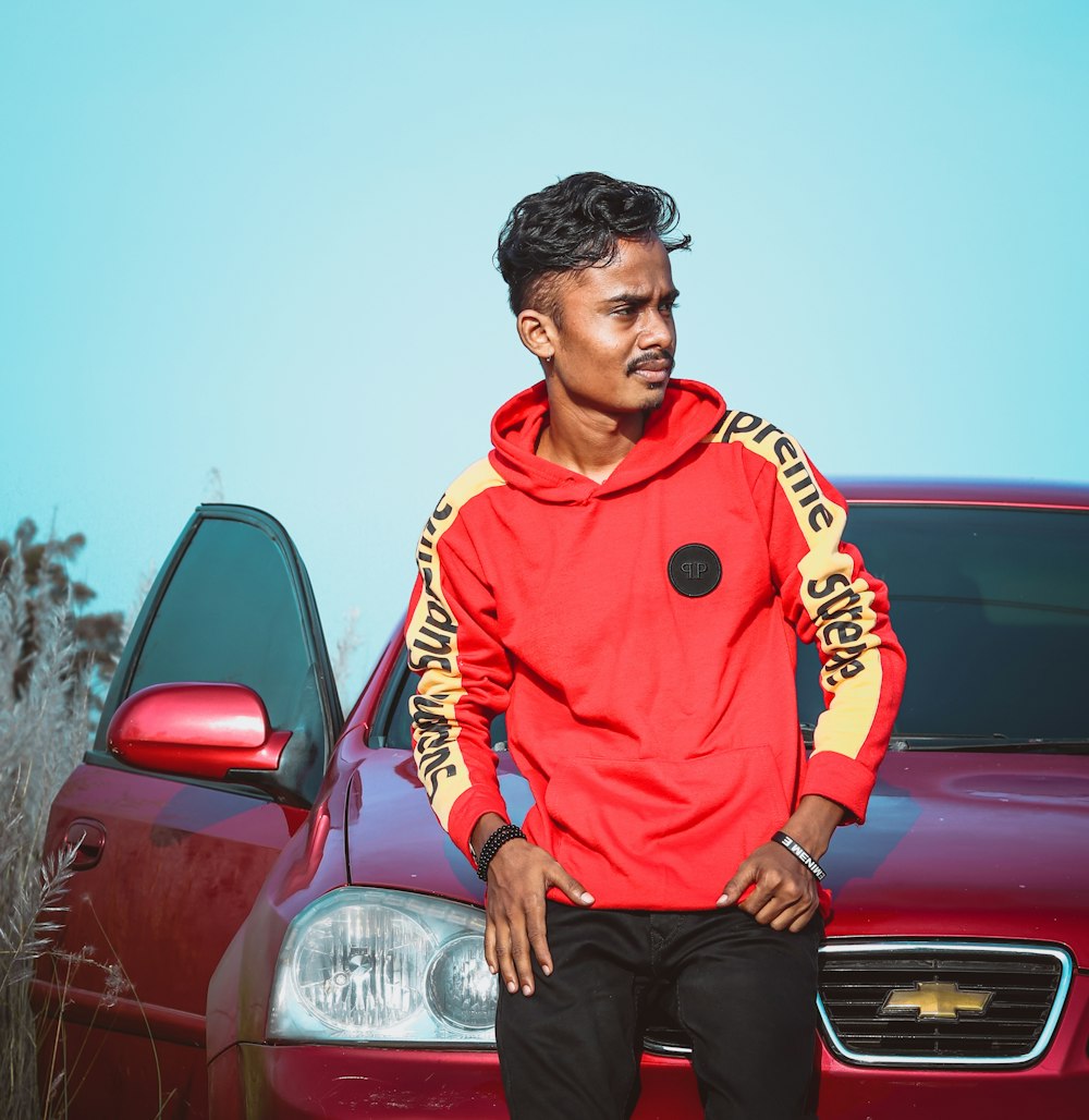 man in red and white zip up hoodie sitting on red car