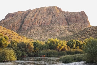 person riding on boat on river near brown mountain during daytime