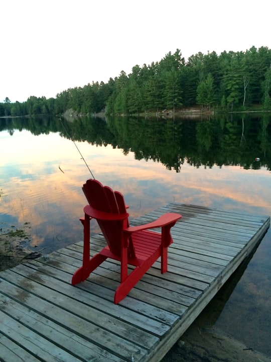 red wooden armchair on dock near lake during daytime in Huntsville Canada