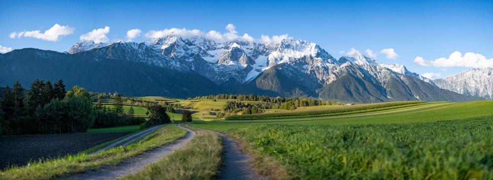 campo de grama verde perto da montanha sob nuvens brancas e céu azul durante o dia