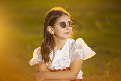 A child sitting in a sunny park, showcasing light pink frame glasses.