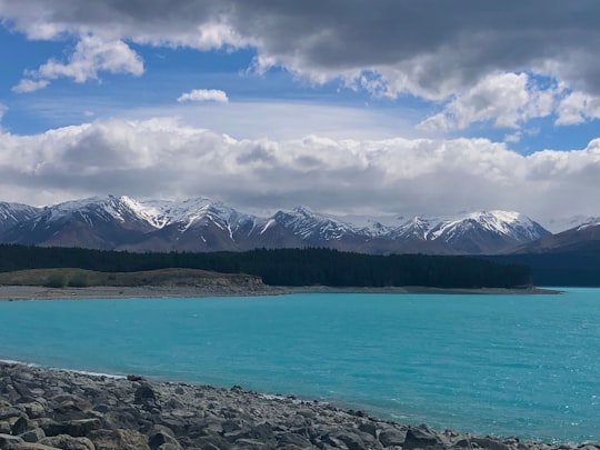 body of water near mountain under white clouds and blue sky during daytime in Mackenzie District New Zealand