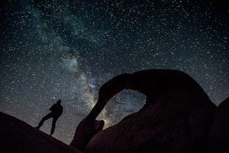 silhouette of man and woman standing on rock formation during night time