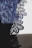 Intricate lace fabric with detailed floral patterns in a deep blue shade is displayed, revealing the fine texture and craftsmanship. The fabric is set against a contrasting light background, emphasizing the delicate design.
