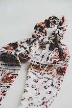 A patterned textile scarf in shades of cream, brown, and black, intricately twisted together, set against a plain white background, creating a visually appealing design.