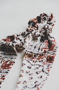 A patterned textile scarf in shades of cream, brown, and black, intricately twisted together, set against a plain white background, creating a visually appealing design.