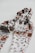 A patterned textile scarf in shades of cream, brown, and black, intricately twisted together, set against a plain white background, creating a visually appealing design.