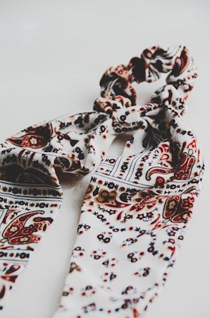 A patterned textile scarf in shades of cream, brown, and black, intricately twisted together, set against a plain white background, creating a visually appealing design.