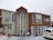 A two-story building with large windows is surrounded by snow. The structure is constructed with a mix of light-colored and wooden panels. A sign displaying 'HAKA LODGE Backpackers' is visible on the right side. Snow is actively falling, and a white vehicle is parked in the front with traffic cones placed nearby.