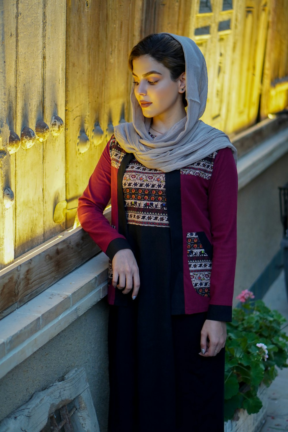 Frau in rotem langärmeligem Kleid mit braunem Hijab steht tagsüber neben einer gelben Holztür