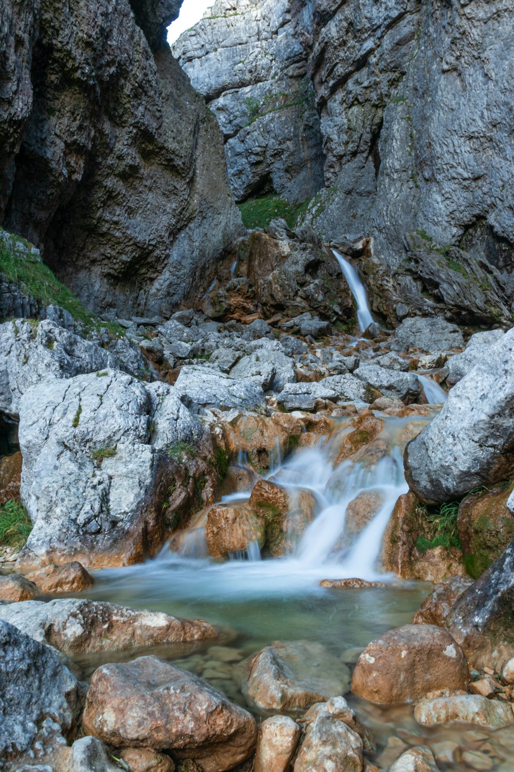 water falls between gray rocky mountain during daytime