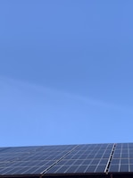 A clear blue sky above a row of solar panels installed at an angle. The panels are composed of a grid of cells, suggesting they are used for capturing solar energy.