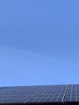A clear blue sky above a row of solar panels installed at an angle. The panels are composed of a grid of cells, suggesting they are used for capturing solar energy.