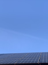 A clear blue sky above a row of solar panels installed at an angle. The panels are composed of a grid of cells, suggesting they are used for capturing solar energy.