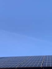 A clear blue sky above a row of solar panels installed at an angle. The panels are composed of a grid of cells, suggesting they are used for capturing solar energy.