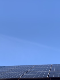 A clear blue sky above a row of solar panels installed at an angle. The panels are composed of a grid of cells, suggesting they are used for capturing solar energy.
