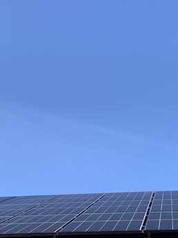 A clear blue sky above a row of solar panels installed at an angle. The panels are composed of a grid of cells, suggesting they are used for capturing solar energy.