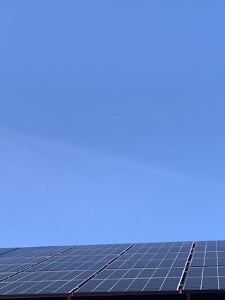 A clear blue sky above a row of solar panels installed at an angle. The panels are composed of a grid of cells, suggesting they are used for capturing solar energy.