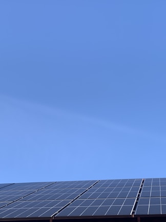 A clear blue sky above a row of solar panels installed at an angle. The panels are composed of a grid of cells, suggesting they are used for capturing solar energy.