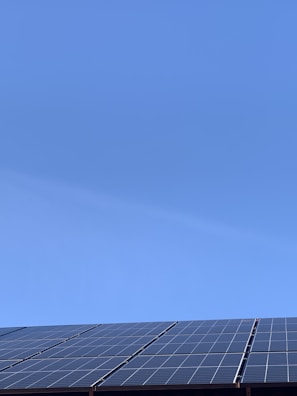 A clear blue sky above a row of solar panels installed at an angle. The panels are composed of a grid of cells, suggesting they are used for capturing solar energy.