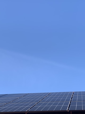 A clear blue sky above a row of solar panels installed at an angle. The panels are composed of a grid of cells, suggesting they are used for capturing solar energy.