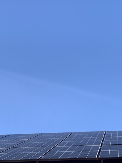 A clear blue sky above a row of solar panels installed at an angle. The panels are composed of a grid of cells, suggesting they are used for capturing solar energy.