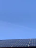A friendly solar panel technician smiling while checking solar panels under a bright blue sky.