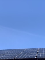 A clear blue sky above a row of solar panels installed at an angle. The panels are composed of a grid of cells, suggesting they are used for capturing solar energy.
