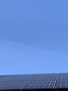 A clear blue sky above a row of solar panels installed at an angle. The panels are composed of a grid of cells, suggesting they are used for capturing solar energy.