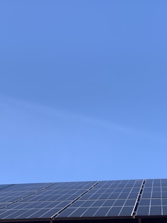 A clear blue sky above a row of solar panels installed at an angle. The panels are composed of a grid of cells, suggesting they are used for capturing solar energy.