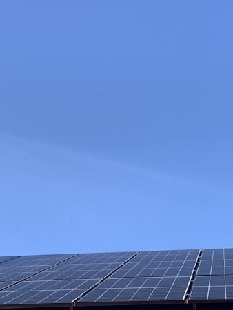 A clear blue sky above a row of solar panels installed at an angle. The panels are composed of a grid of cells, suggesting they are used for capturing solar energy.