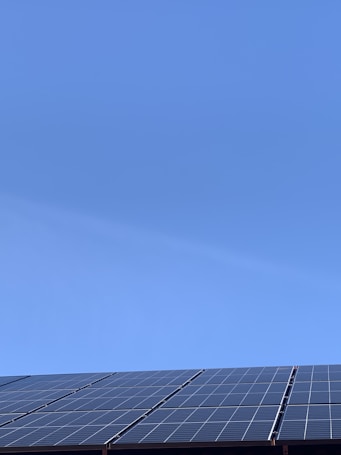 A clear blue sky above a row of solar panels installed at an angle. The panels are composed of a grid of cells, suggesting they are used for capturing solar energy.