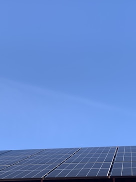 A clear blue sky above a row of solar panels installed at an angle. The panels are composed of a grid of cells, suggesting they are used for capturing solar energy.
