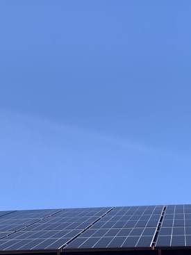 A clear blue sky above a row of solar panels installed at an angle. The panels are composed of a grid of cells, suggesting they are used for capturing solar energy.