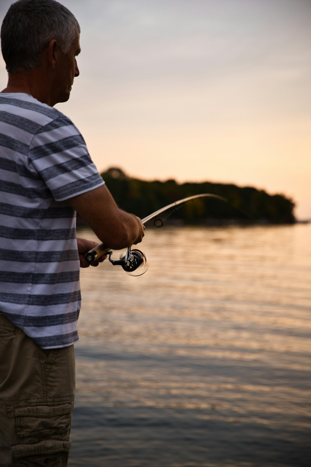 man in white and blue stripe shirt and gray shorts holding black and silver fishing rod