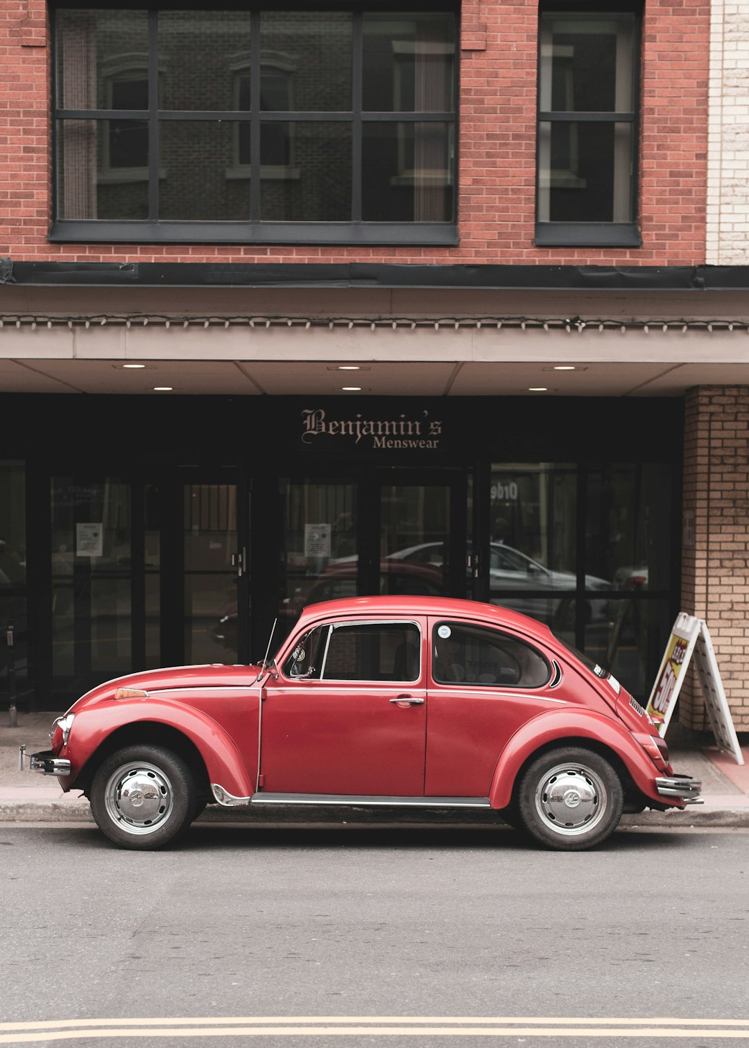 red volkswagen beetle parked beside brown concrete building during daytime