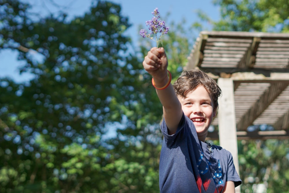 boy in blue crew neck t-shirt holding pink flower during daytime