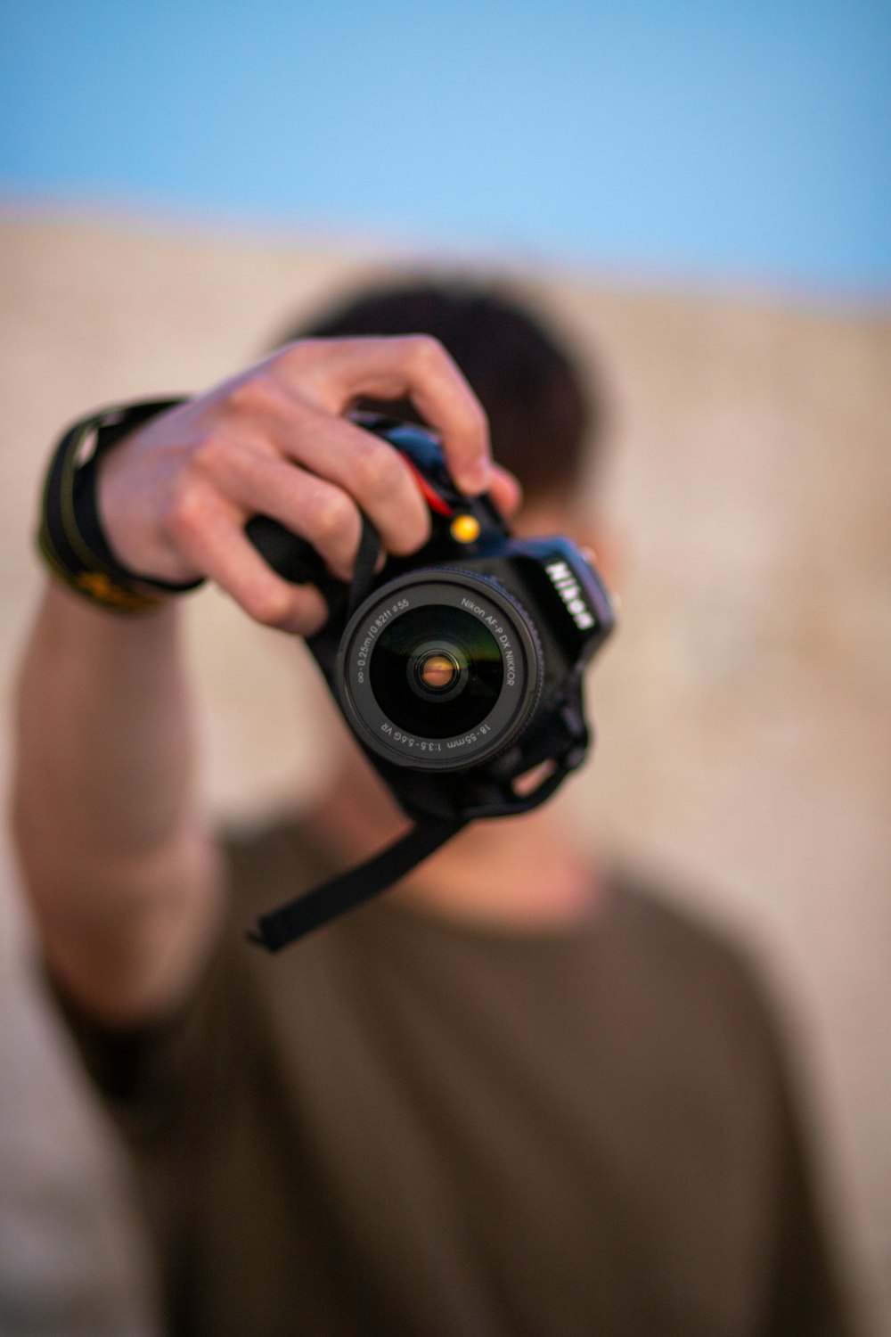 man in brown crew neck t-shirt holding black nikon dslr camera