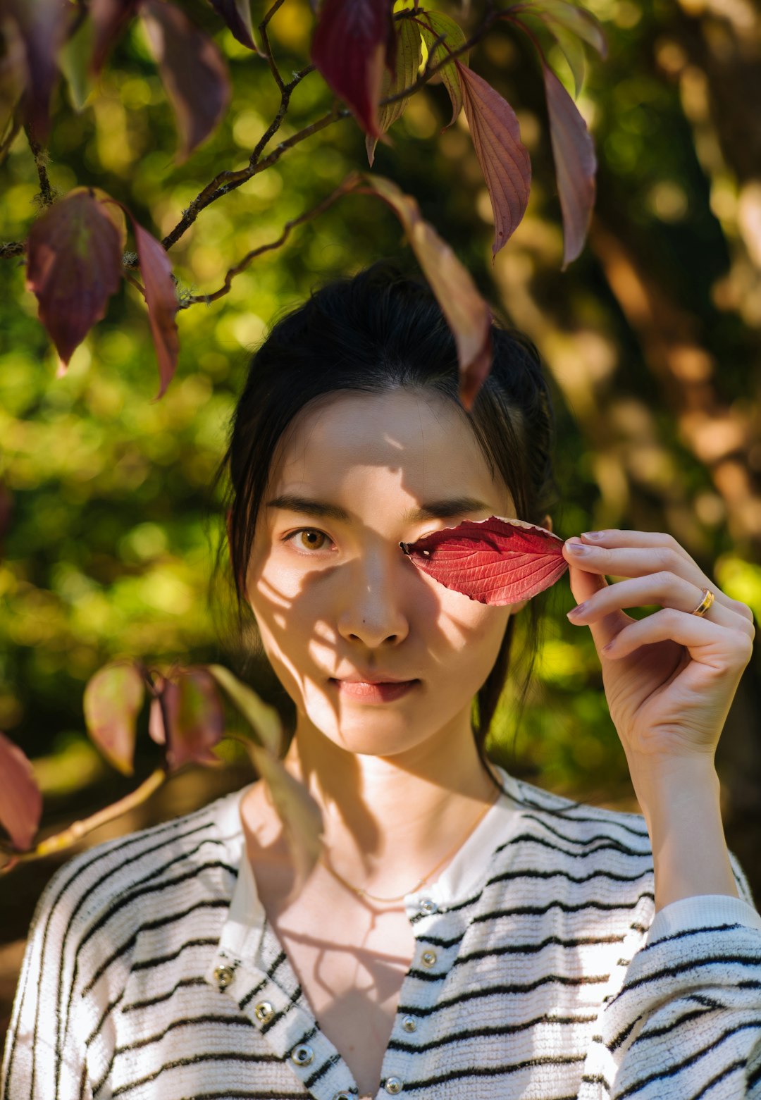 woman in white and black stripe shirt holding red leaf