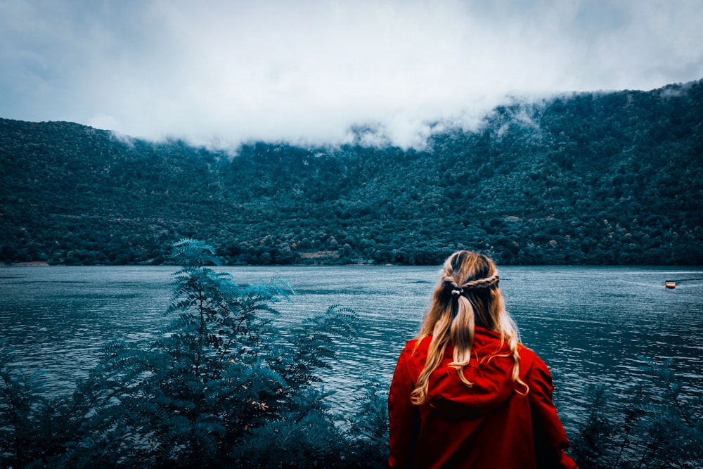 woman in red jacket standing near body of water during daytime