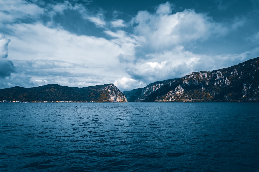 green and brown mountain beside body of water under white clouds and blue sky during daytime