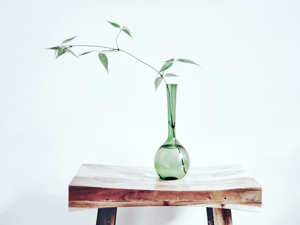 Jarrón de vidrio verde sobre mesa de madera marrón