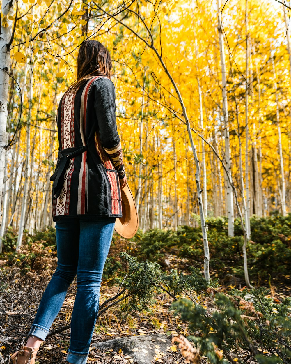 woman in black leather jacket and blue denim jeans standing on forest during daytime