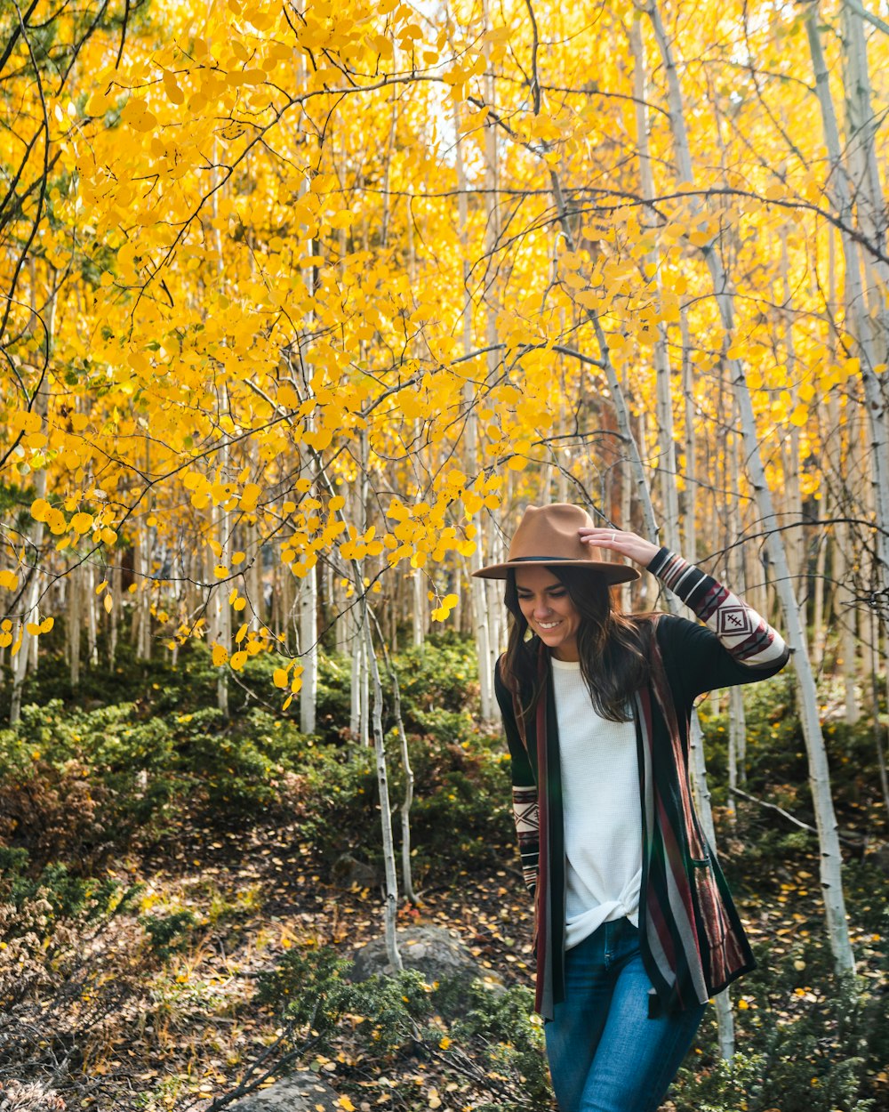 Mujer con camisa blanca de manga larga y sombrero marrón de pie cerca de árboles de hojas amarillas durante el día