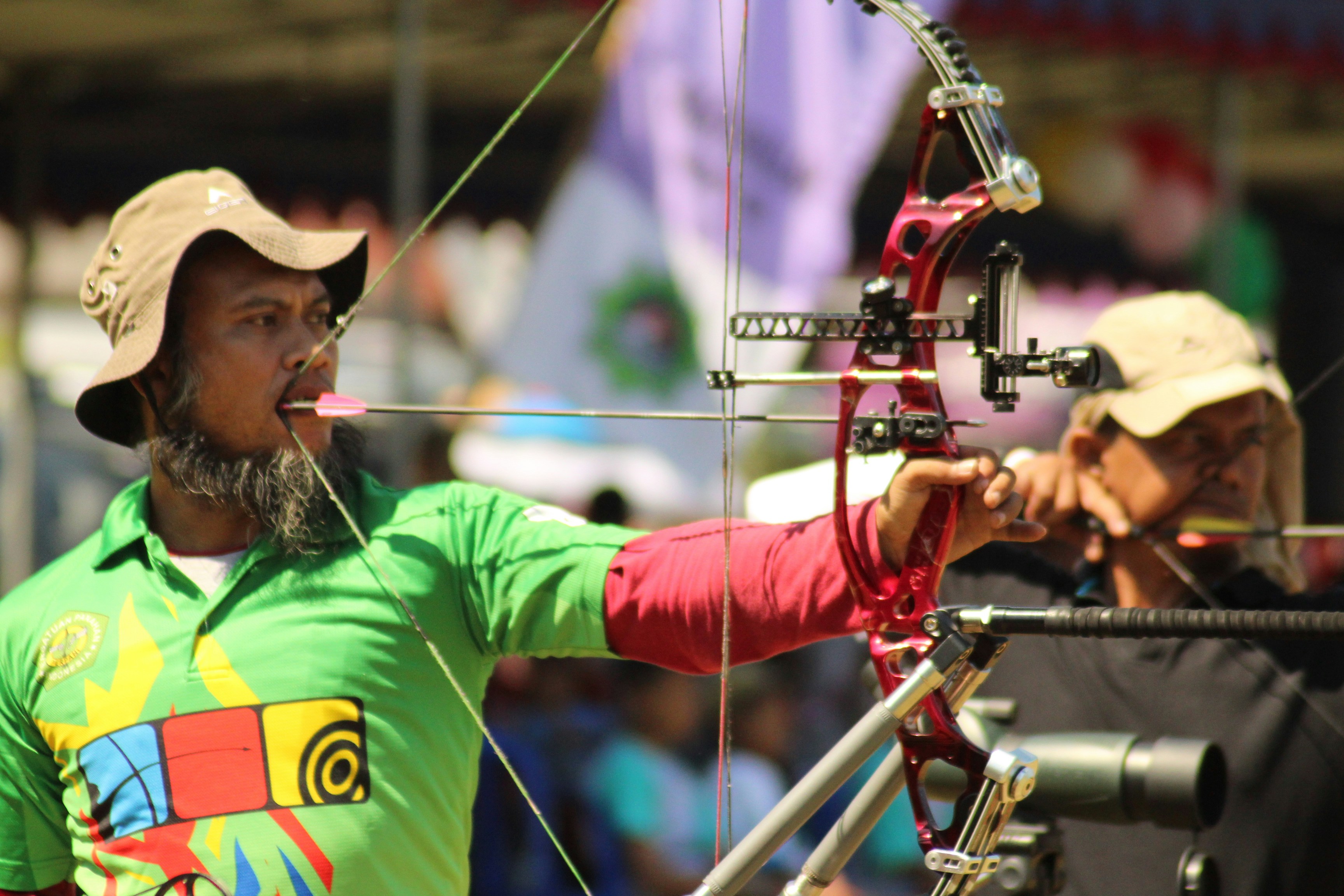 Seorang pria berbaju hijau mengarahkan busur ke target