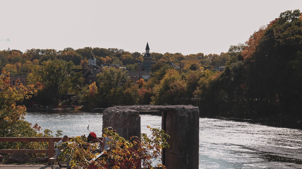 person in red jacket sitting on brown wooden post near body of water during daytime