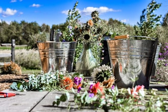 A vibrant bucket filled with a mix of sunflowers, daisies, and greenery, sitting on a rustic wooden table.