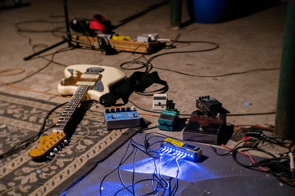 An electric guitar and effects pedalboard placed on the floor of a live music venue at night.